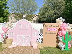 a pink barn with balloons and decorations on the grass near a sign that says rodeo