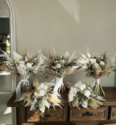 three vases filled with white flowers on top of a wooden table next to a mirror