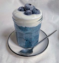 a glass jar filled with blueberries sitting on top of a saucer next to a spoon