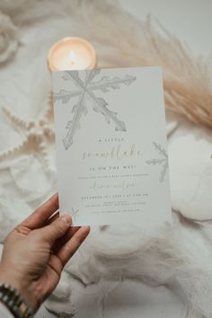 a person holding up a card with a snowflake design on it and a lit candle in the background