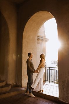 a man and woman holding hands while standing in an archway with the sun shining through