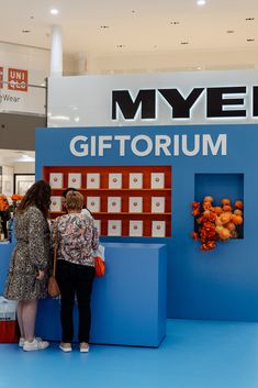 two women standing in front of a blue booth with orange flowers on it's sides