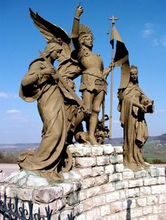 three statues on top of a brick wall with a sky in the backround