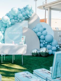 a table with balloons on it in front of a white wall and green grass area