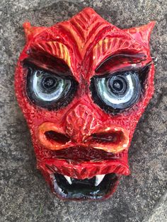 This ceramic wall hanging depicts a dragon face in celebration of the Chinese Lunar New Year and year of the wood dragon.  Created from a thick slab of clay, the mask depicts a large-eyed dragon with viscous teeth. The red glazed surface is heavily textured and has accents in yellow, grey, black and white.  Wire is attached on each side for hanging on a wall. The mask is 6" x 4.5" x 1.5". Wood Dragon, Chinese Lunar New Year, Ceramic Mask, Ceramic Wall Hanging, Dragon Face, Mask Wall, Yellow Grey, Year Of The Dragon, Lunar New Year