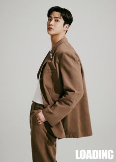 a young man standing in front of a white background wearing a brown coat and slacks