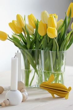 a vase filled with yellow tulips next to a candle and some rocks on a table