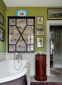 a bathroom with green walls and pictures on the wall, including a claw foot bathtub