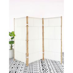 a room divider made out of bamboo sticks and white fabric, with a potted plant in the corner