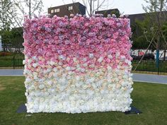 an artificial flower wall in the middle of a park with lots of pink and white flowers on it