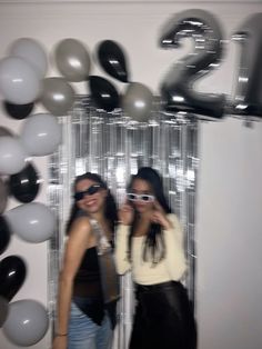 two women standing next to each other in front of balloons and numbers on the wall