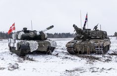 two tanks are sitting in the snow with flags sticking out of them and one is camouflaged