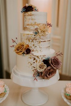 a three tiered white cake with flowers on the side and gold flecks