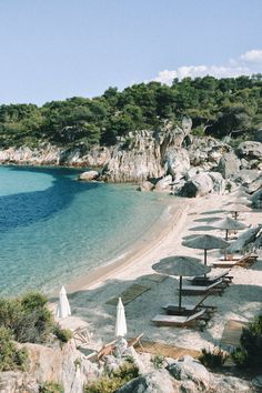 an empty beach with umbrellas and chairs on the sand by the water's edge