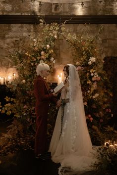 a bride and groom standing in front of a flower covered wall at their wedding ceremony