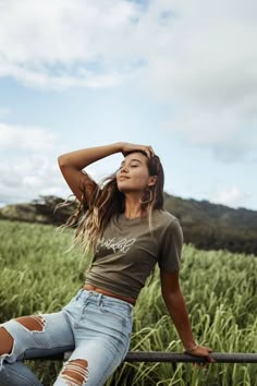 a woman sitting on top of a rail next to a field of green grass with her hands behind her head