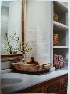 a bathroom sink sitting under a mirror next to a wooden shelf filled with towels and plants