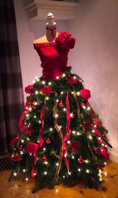 a dress made out of christmas tree with lights on it and red flowers in the skirt