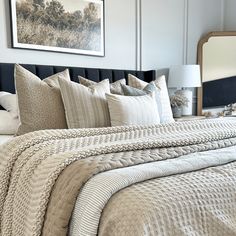 a bed with white and beige comforters in a bedroom next to a painting on the wall