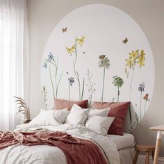 a bed with white sheets and red pillows in front of a wall mural that has yellow flowers on it