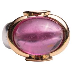 A spectacular large pink tourmaline cabochon dome ring set in 18K gold. It is flanked by two marquise cut tanzanite stones also set in 18K gold. The band itself is sterling silver. Ring size is 7.25. The fine jewelry collection is sourced, designed or created by Deborah Lockhart Phillips. Through her international travels, she has cultivated prime resources for fine precious and semi-precious gemstones of unusual cuts in a variety of settings. Included in the collection are antique, high 22K gol Luxury Tourmaline Jewelry In Oval Cabochon Shape, Luxury Tourmaline Oval Cabochon Jewelry, Luxury Tourmaline Jewelry With Oval Cabochon, Pink Gold Oval Ruby Ring With Gemstone, Tanzanite Stone, Dome Ring, Domed Ring, Fine Jewelry Collection, Marquise Cut