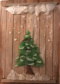 a christmas tree made out of plastic bottle caps on a wooden board with snow around it