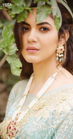 a woman in a green and gold sari with leaves on her head, posing for the camera