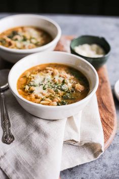 two bowls of soup are sitting on a wooden board with silverware and spoons