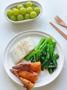 a white plate topped with meat and veggies next to a bowl of grapes