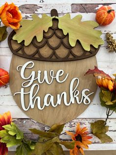 a wooden sign that says give thanks surrounded by fall leaves and flowers on a white wood background