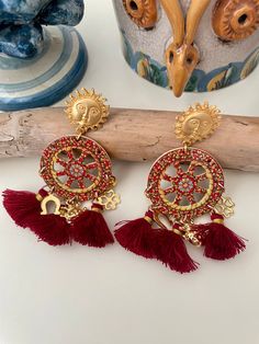 ✔️ Eye-catching Sicilian dangling earrings! Made with a brass pin in the shape of the Sun, a reference to the beautiful Sicily, a wooden cart wheel colored mainly in orange and yellow, three burgundy red cotton tassels and assorted charms, symbols of Superstition and Luck. A very impressive jewel, wearing it you will never go unnoticed! Get ready to amaze with this must-have accessory! ✔️DETAILS: 🟩 Materials: Cotton Wood Brass 🟧🟧 Dimensions: Earrings length: 8.5 cm (3.4") Wheel dimensions: 3. Traditional Red Jewelry With Tassels, Red Tasseled Jewelry For Gift, Red Tasseled Jewelry As A Gift, Festival Gift Jewelry With Tassels, Red Dangle Tassel Earrings As Gift, Red Bohemian Tassel Earrings As Gift, Red Dangle Tassel Earrings For Gift, Red Tassel Earrings For Gift, Red Tassel Drop Earrings Gift