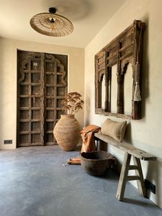 a wooden bench sitting in the middle of a room next to a vase and mirror