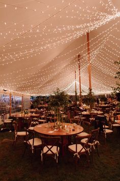 tables and chairs are set up under a tent with lights strung from the ceiling over them