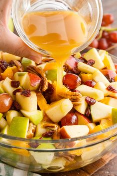 someone pouring dressing into a bowl of fruit salad