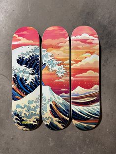 three skateboards with the same painting on them, one has an ocean wave in it