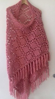 a pink crocheted shawl with fringes hanging on a white wall next to a coat hanger