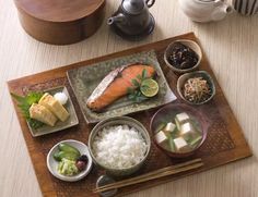 a wooden tray topped with different types of food on top of a table next to a tea pot