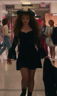 a woman in a black dress and hat walking through an airport