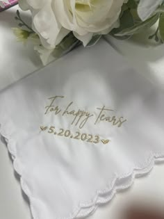 a white handkerchief with the words happy tears embroidered on it next to a bouquet of flowers