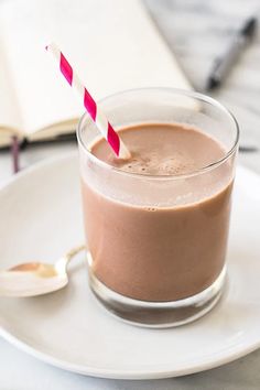 a chocolate drink with a striped straw in a glass on a plate next to an open book