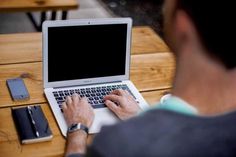 a man sitting at a table using a laptop computer with his cell phone next to him