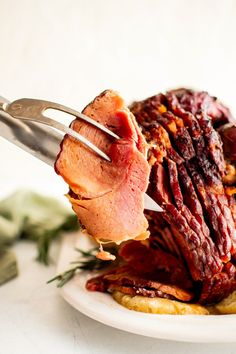 a person holding a fork with meat on top of it and another piece of food in the background