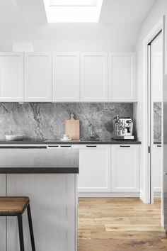 a kitchen with white cabinets and marble counter tops, two stools in front of the island