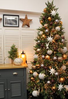 a decorated christmas tree with gold and silver ornaments on it in front of shutters