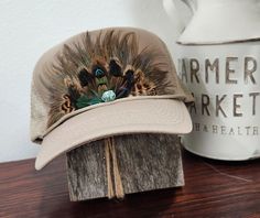 Introducing the Feather Crown Western Retro Trucker Hat You  will adore this 1970s-inspired trucker hat, complete with a unique feather design that distinguishes each piece.  Additional features: Snap Closure Light-weight, foam-constructed front 5-panel design  High profile  Curved visor and semi-structured crown One Size fits all Feathers affixed with glue and the turquoise bead stitched Each hat is handmade and one-of-a-kind Choice of hat colors: Khaki Cowboy, Rodeo, Western, Country, Trucker Hat, Embellished Hat, retro Trucker Hat, Western Trucker Hat, Rodeo Hat, Western Wear, Feather Hat band hat Vintage Brown Trucker Hat For Spring, Brown Trucker Hat With Short Brim For Spring, Brown Short Brim Trucker Hat For Spring, Spring Brown Trucker Hat With Short Brim, Vintage Adjustable Mini Hats With Feathers, Vintage Adjustable Mini Hat With Feathers, Adjustable Beige Hat With Feathers, Vintage Festival Hat With Feathers, Spring Beige Hat With Feathers