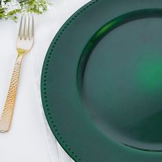 a green plate with a gold fork on it next to a white table cloth and flowers