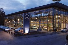 a mercedes benz dealership at night with cars parked in the parking lot behind it