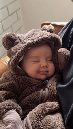 a baby wrapped in a bear costume sleeping on someone's lap with his eyes closed