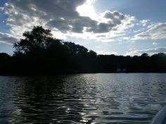 the sun shines brightly through clouds over a body of water with trees in the background