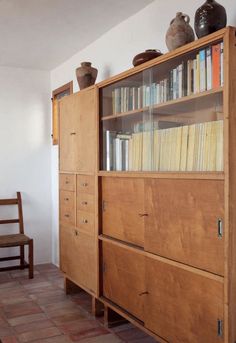 a wooden cabinet with books and vases on it's top shelf next to a chair